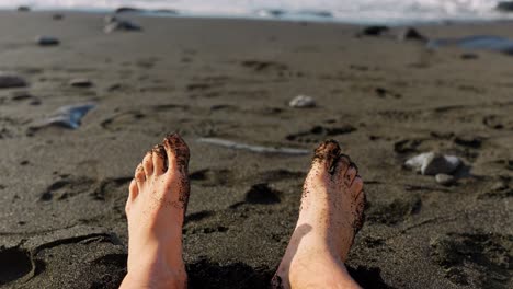 pov detail close up of relaxed feet at beach with black sand on toes, tenerife