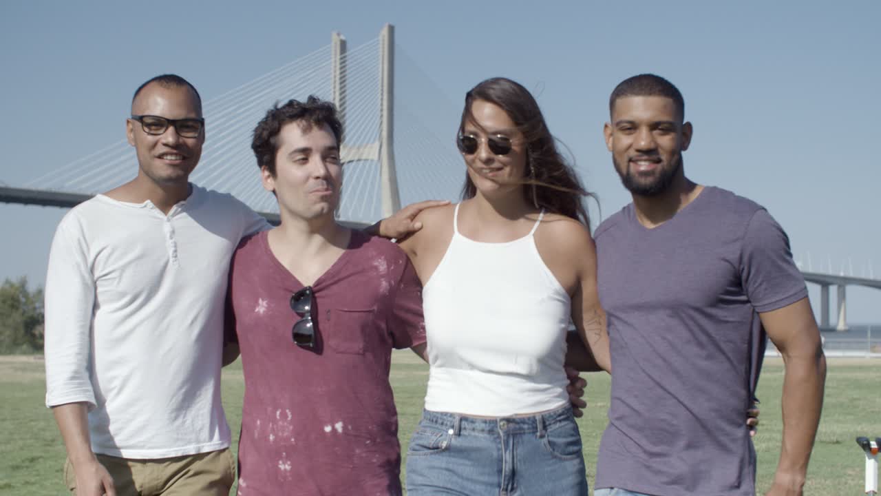 vista frontal de amigos sonrientes abrazándose y caminando por el prado.