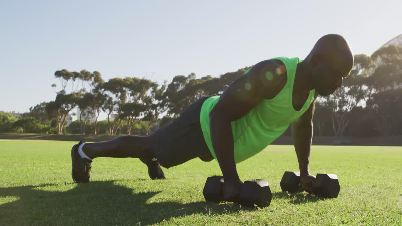 Fit african american man exercising outdoors doing press ups holding dumbbells