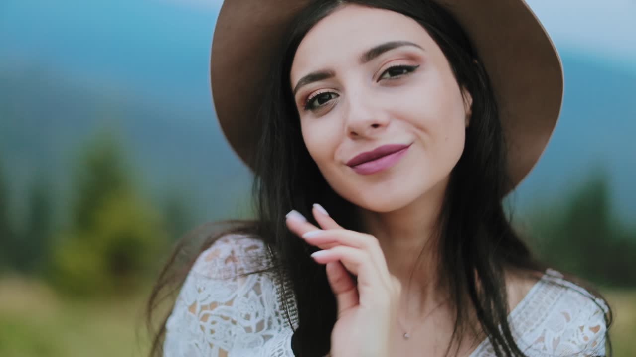 Portrait shot of attractive girl outdoors. Beautiful dark-haired woman in hat looking at camera and positively smiling.