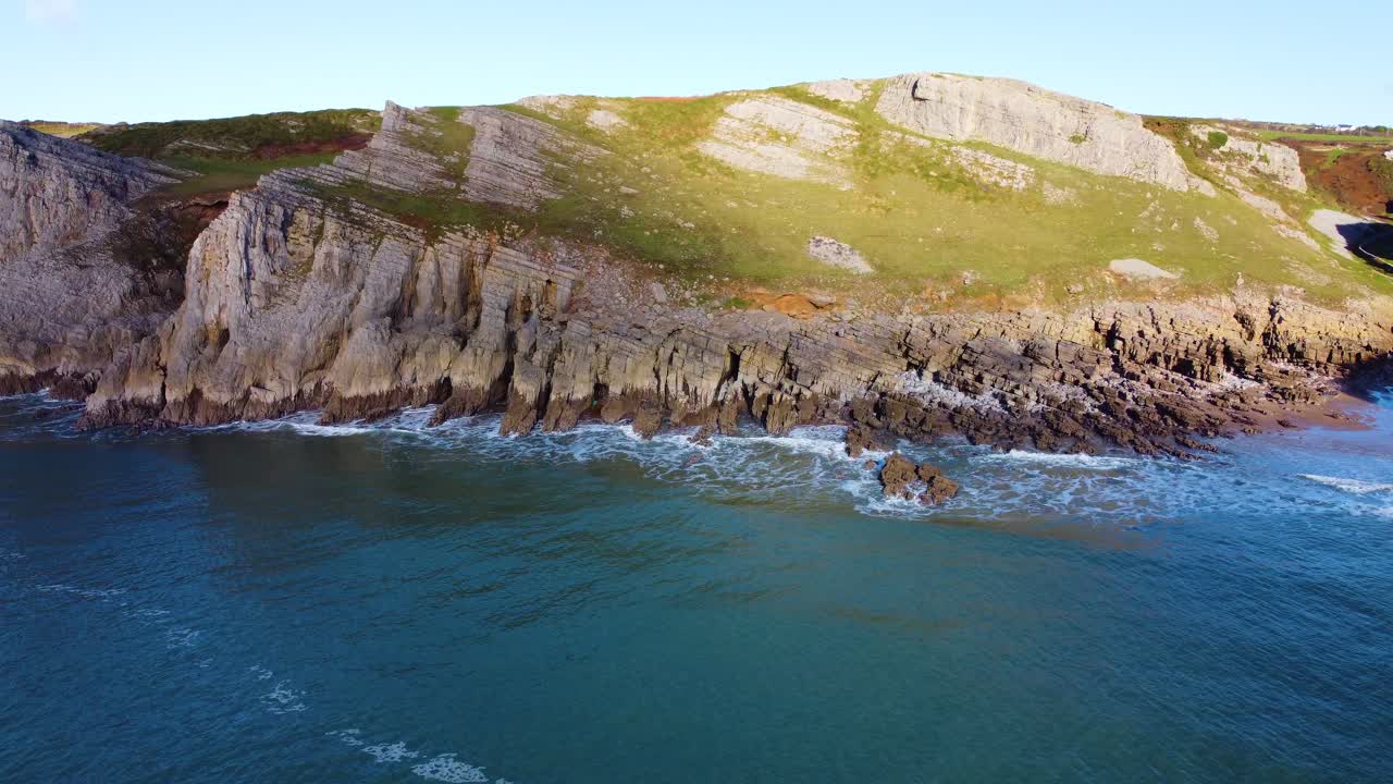 Aerial Reveal Over Sea of Small Rocky Beach with Deep Steep Valley Behind with Sun Shining Down on Cliffs with Exposed Natural Rock