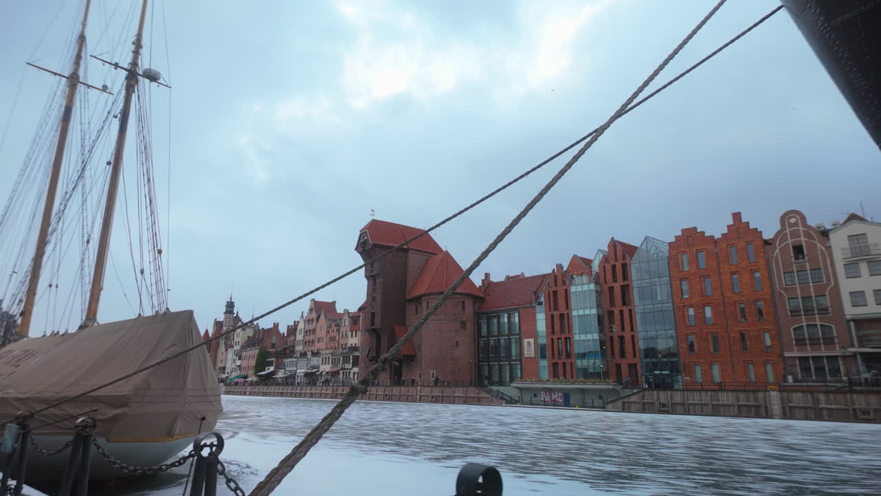 En naturskøn udsigt over den historiske middelalderlige kran og farverige lejlighedsbygninger i Gdansk gamle bydel, set fra en båd på den frosne Motlawa-flod