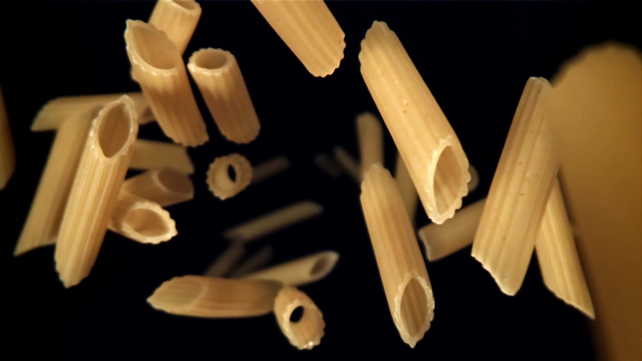 Rohe Penne-Nudeln fallen in Zeitlupe auf schwarzem Hintergrund