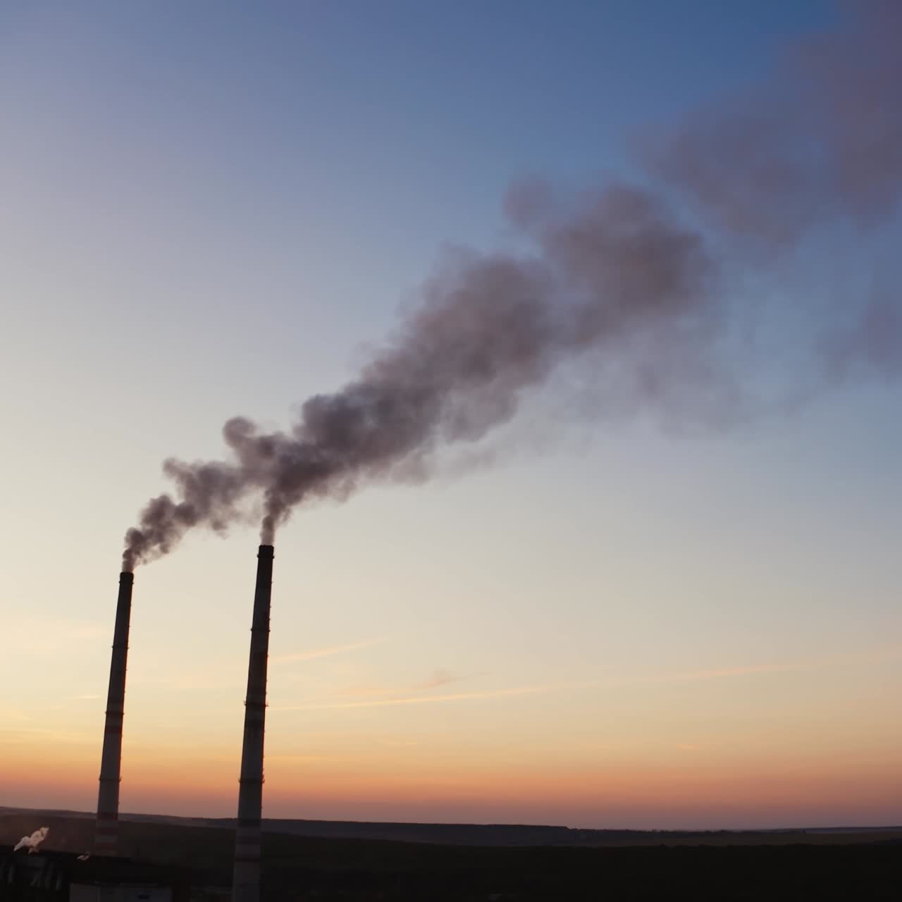 Pipes with smoke on the evening sky background. Harmful smoke going into the air from two industrial pipes of a factory at sunset.