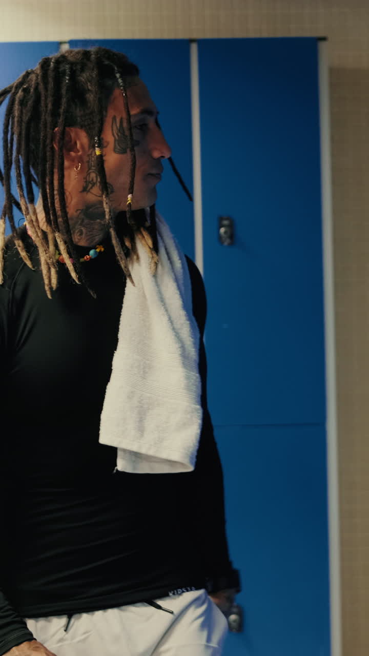 Mand med dreadlocks og tatoveringer i omklædningsrum med håndklæde