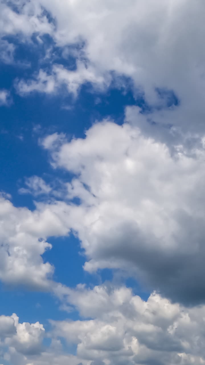 Light cotton clouds transforming in the beautiful blue sky. Quickly moving cloud mass on sunny day. Timelapse. Vertical video