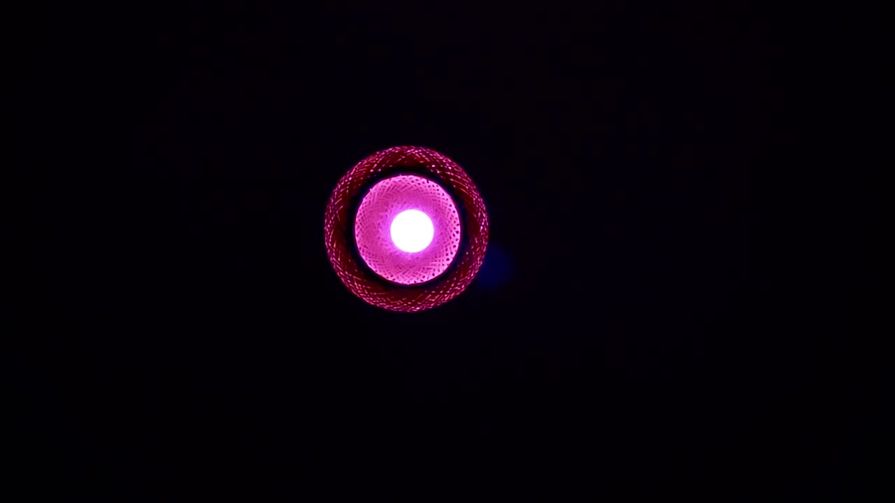 Luce rossa e rosa di una lampada al centro dell'inquadratura, oscurità circostante, statica