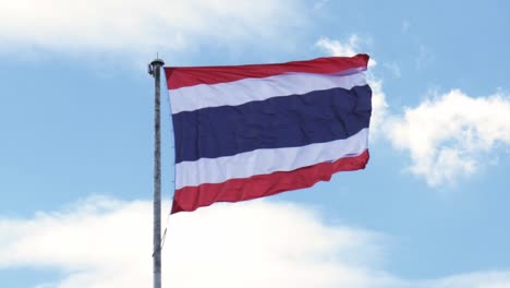 Waving-the-Kingdom-of-Thailand-flag-on-a-pole-with-blue-sky-and-white-clouds-in-the-background