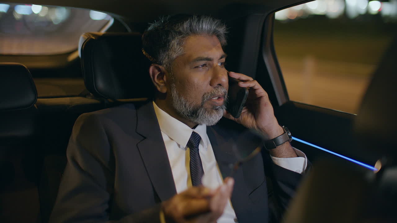 Mature Businessman Speaking on Mobile Phone in Backseat of Car