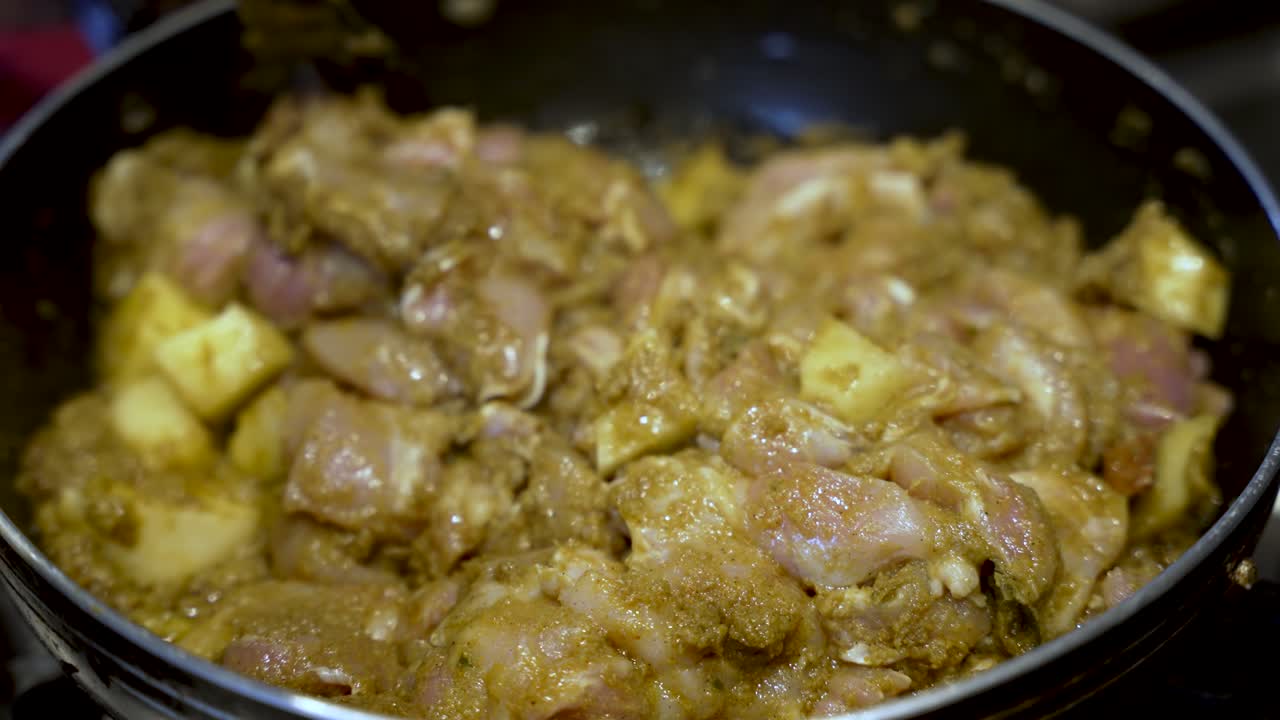 agitar pollo y curry de patatas en una sartén, escena de cocina en casa, iluminación cálida de la cocina
