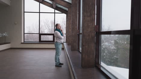 a man stands by a large window looking out and thinking