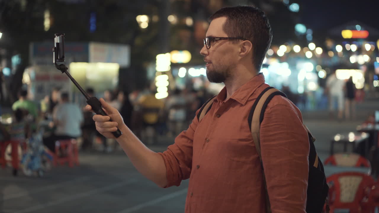 hombre filmando video con un palo de selfie en el mercado nocturno