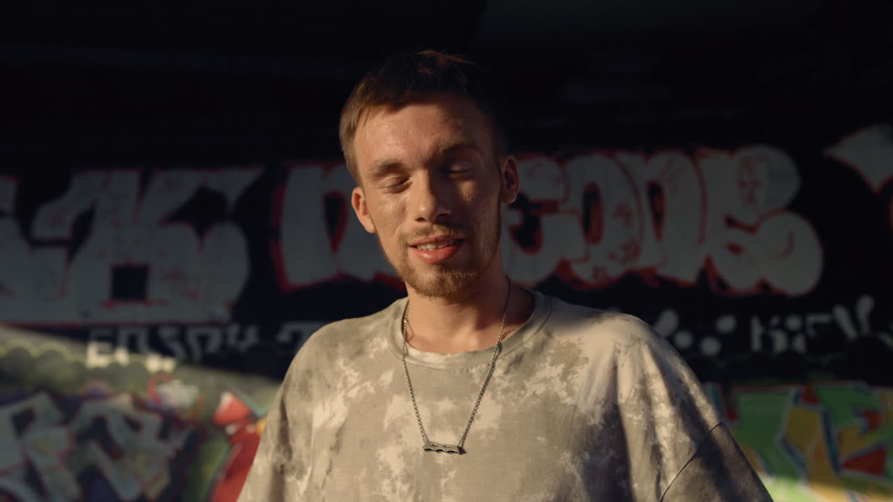 그래피티 벽이 있는 스케이트 파크에서 눈을  ⁇ 이는 행복한 남자. 웃는 롤러 스케이터.