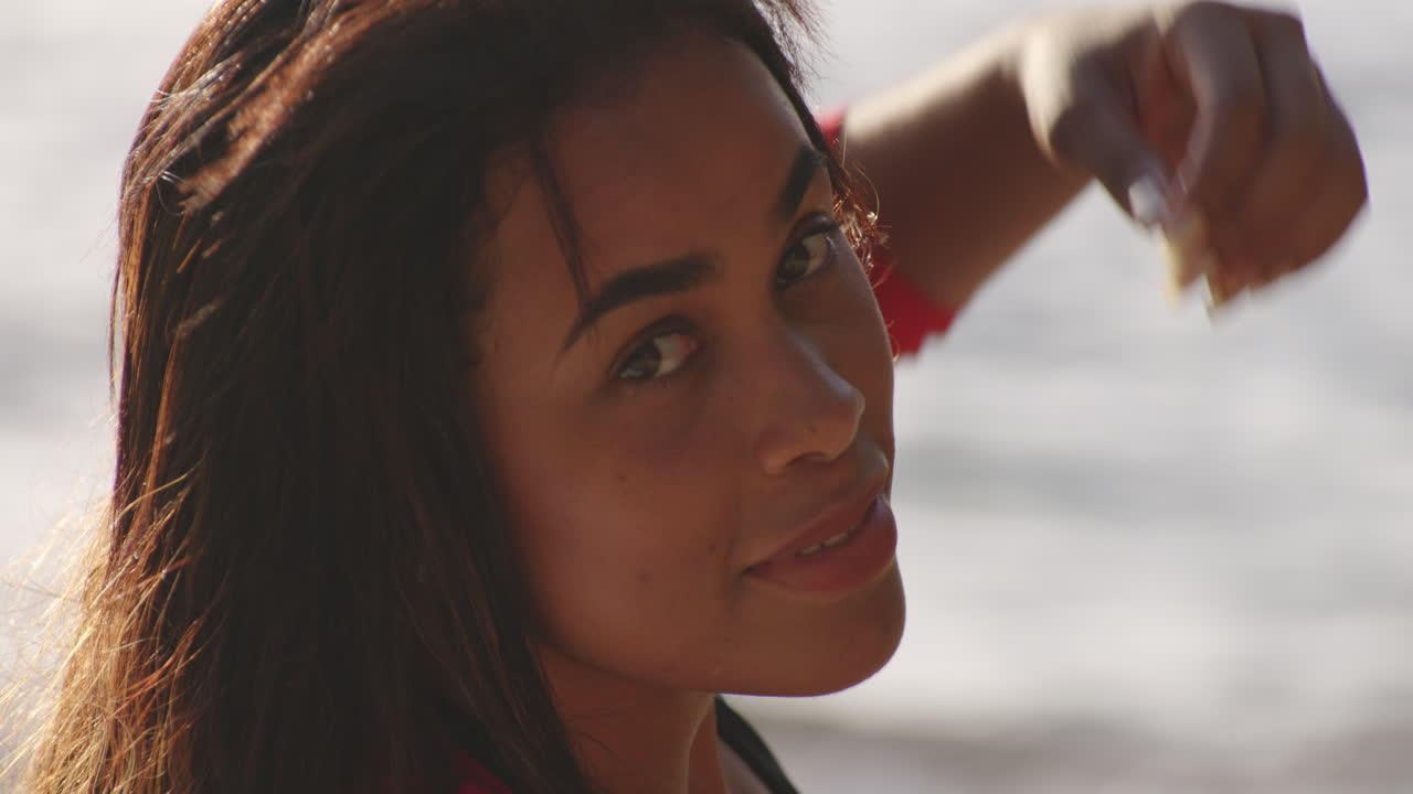 Primo piano del volto di una bella donna latina che si rilassa in spiaggia, si volta e guarda la telecamera.
