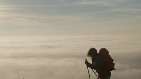 senior woman with backpack climbing mountain with trekking sticks