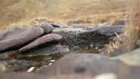 El-Agua-Fluye-Lentamente-Desde-Una-Turbera,-Sobre-Rocas-Y-Baja-Por-Un-Arroyo-De-Montaña-En-Las-Tierras-Altas-De-Escocia