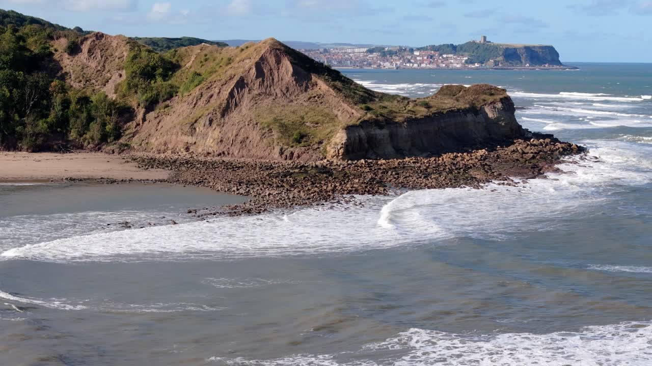 aerial drone footage of Scarborough taken from a distance away over Cayton Bay with blue sky and ocean and big waves