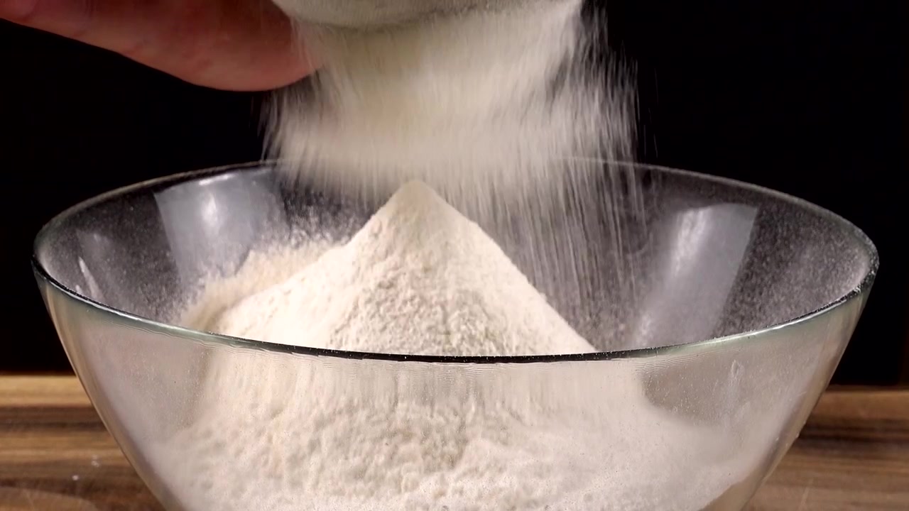 Mengayak tepung menggunakan saringan ke dalam mangkuk kaca di dapur.