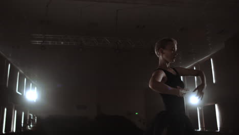 Close-up-of-ballet-dancer-as-she-practices-exercises-on-dark-stage-or-studio.-Ballerina-shows-classic-ballet-pas.-Slow-motion.-Flare-gimbal-shot.