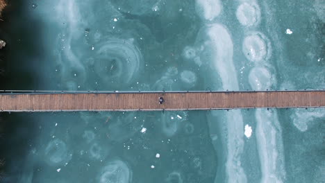 aerial: a man on crutches crosses a wooden bridge over a frozen lake