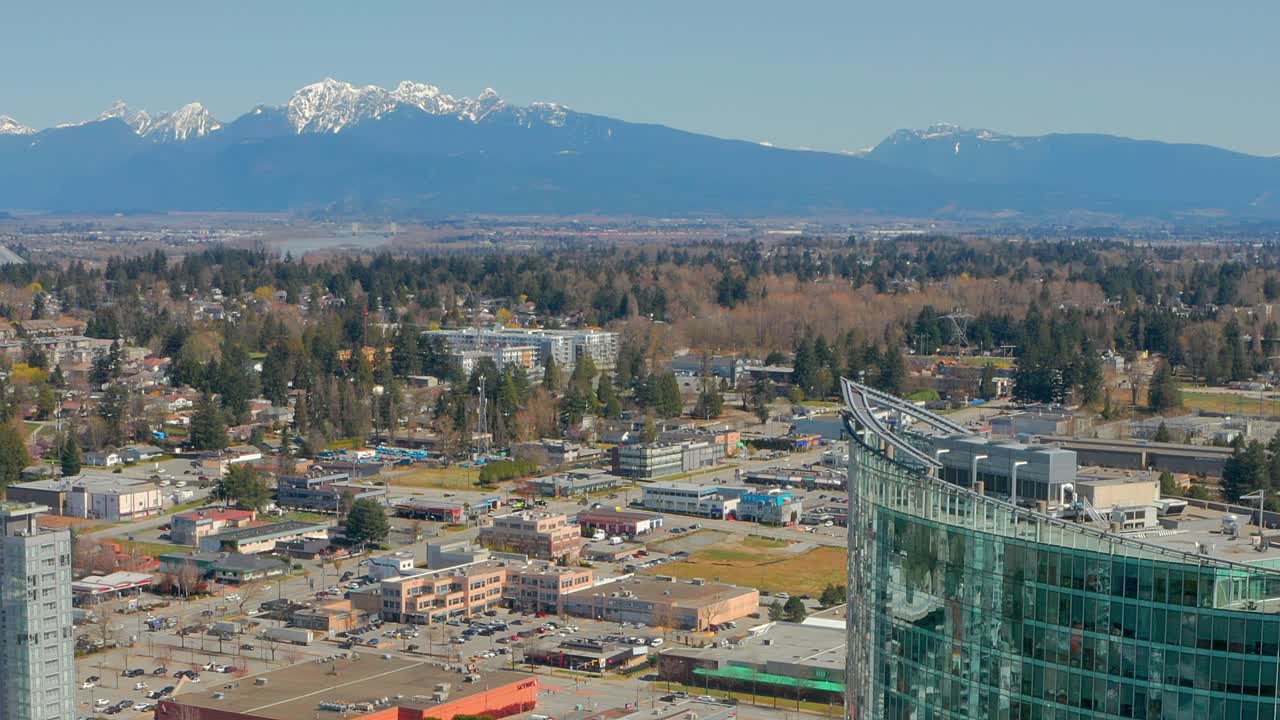 눈 덮인 산은 캐나다 브리티시 컬럼비아 서리에 있는 현대적인 유리 콘도 타워와 병치되어 있습니다.