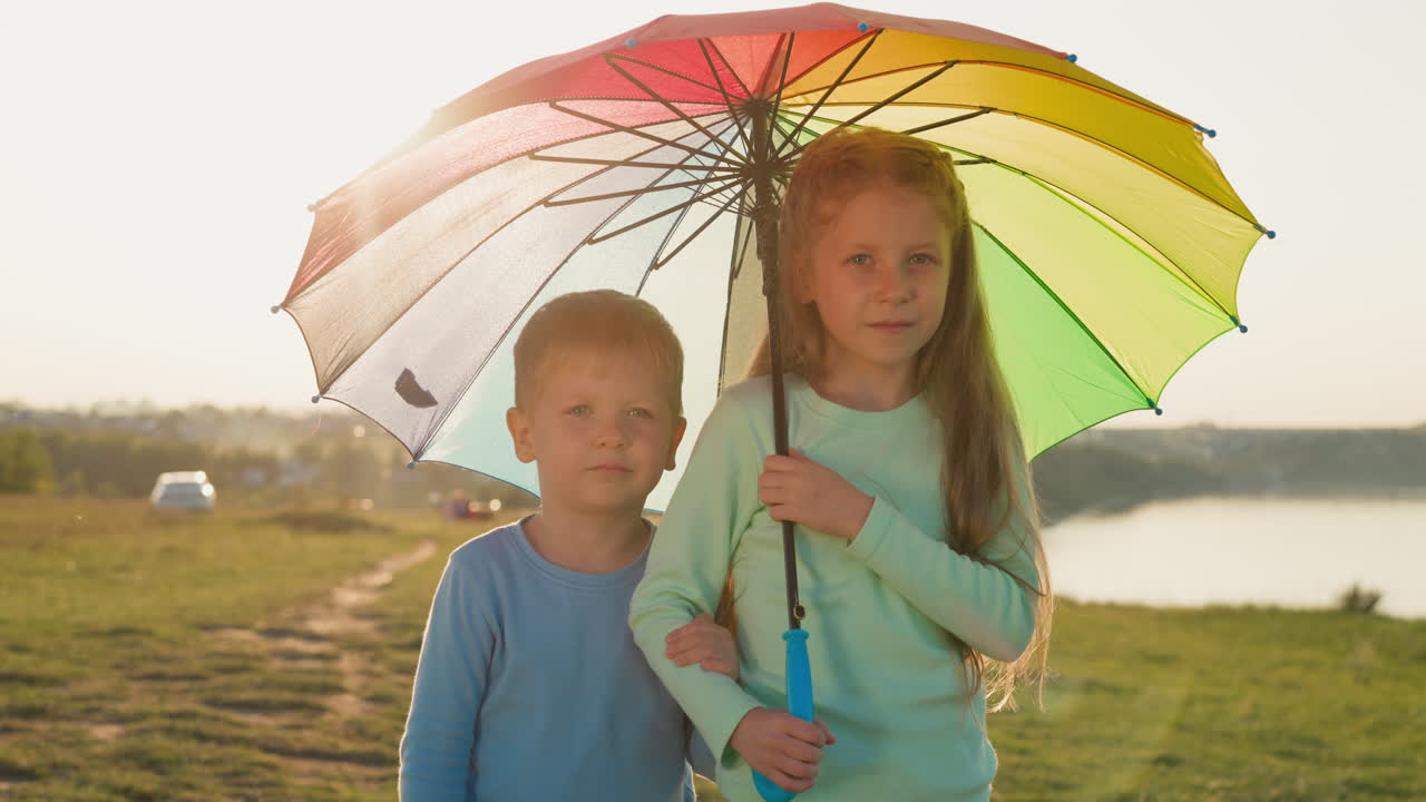los hermanos se acurrucan bajo un paraguas colorido. el hermano y la hermana encantadores encuentran consuelo bajo el vibrante