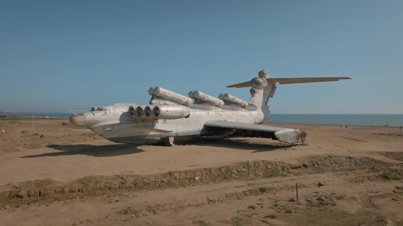Ampia inquadratura dell'ekranoplano sovietico abbandonato di classe Lun su una spiaggia sabbiosa presso il Mar Caspio a Derbent, Repubblica del Daghestan, Russia, sotto un cielo azzurro limpido.