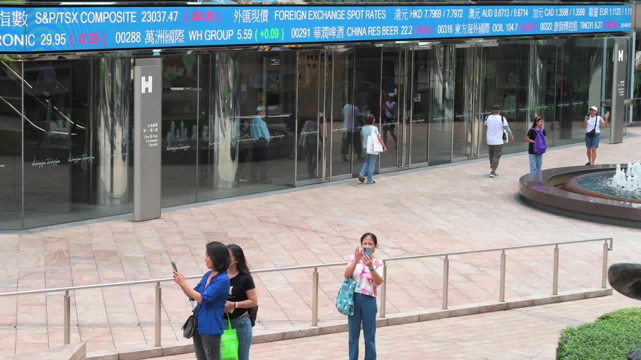 People snap photos as a moving screen in the background shows negative stock ticker symbols at Exchange Square, the home of the Hong Kong Stock Exchange (HKEX), in Hong Kong's financial district.