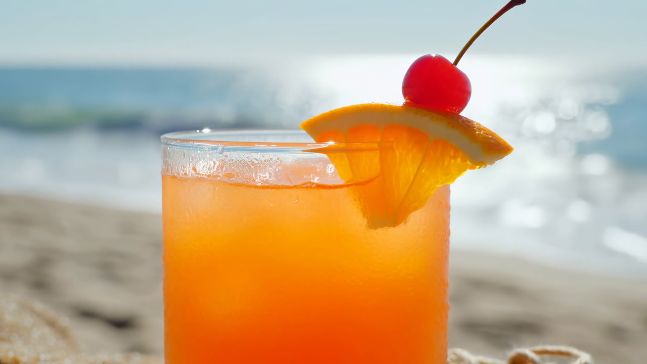 Sunlit Beach Cocktail With Orange Slice, Cherry Garnish, Condensation On Glass And Shimmering Sea