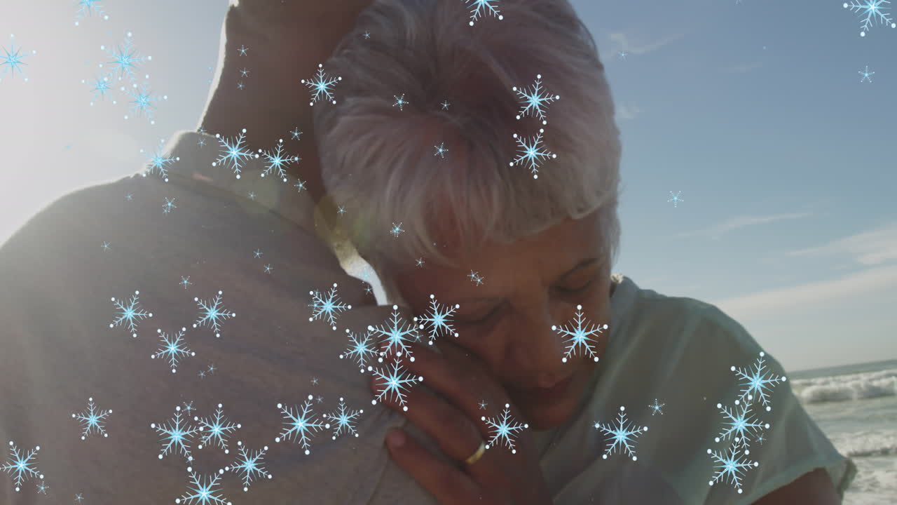 animación de copos de nieve de navidad sobre una pareja de ancianos biracial en la playa