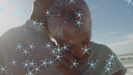 animación de copos de nieve de navidad sobre una pareja de ancianos biracial en la playa
