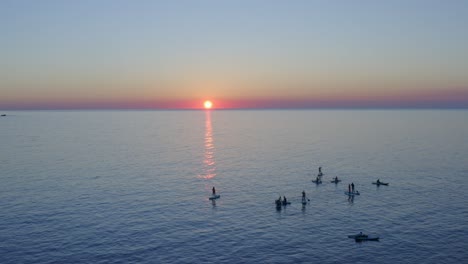 group of paddle boarders on the water at sunset watching the sun set below the horizon