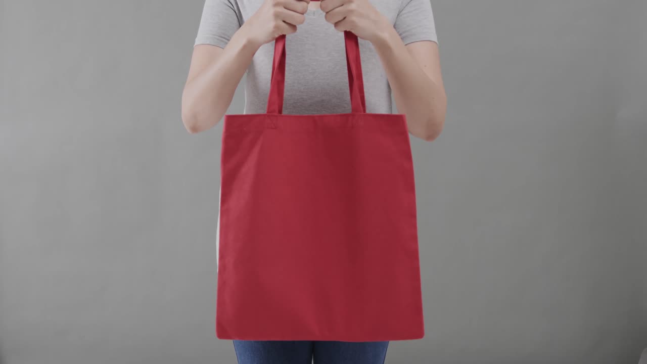 mujer caucásica con camiseta blanca sosteniendo una bolsa roja sobre un fondo gris, espacio de copia, cámara lenta