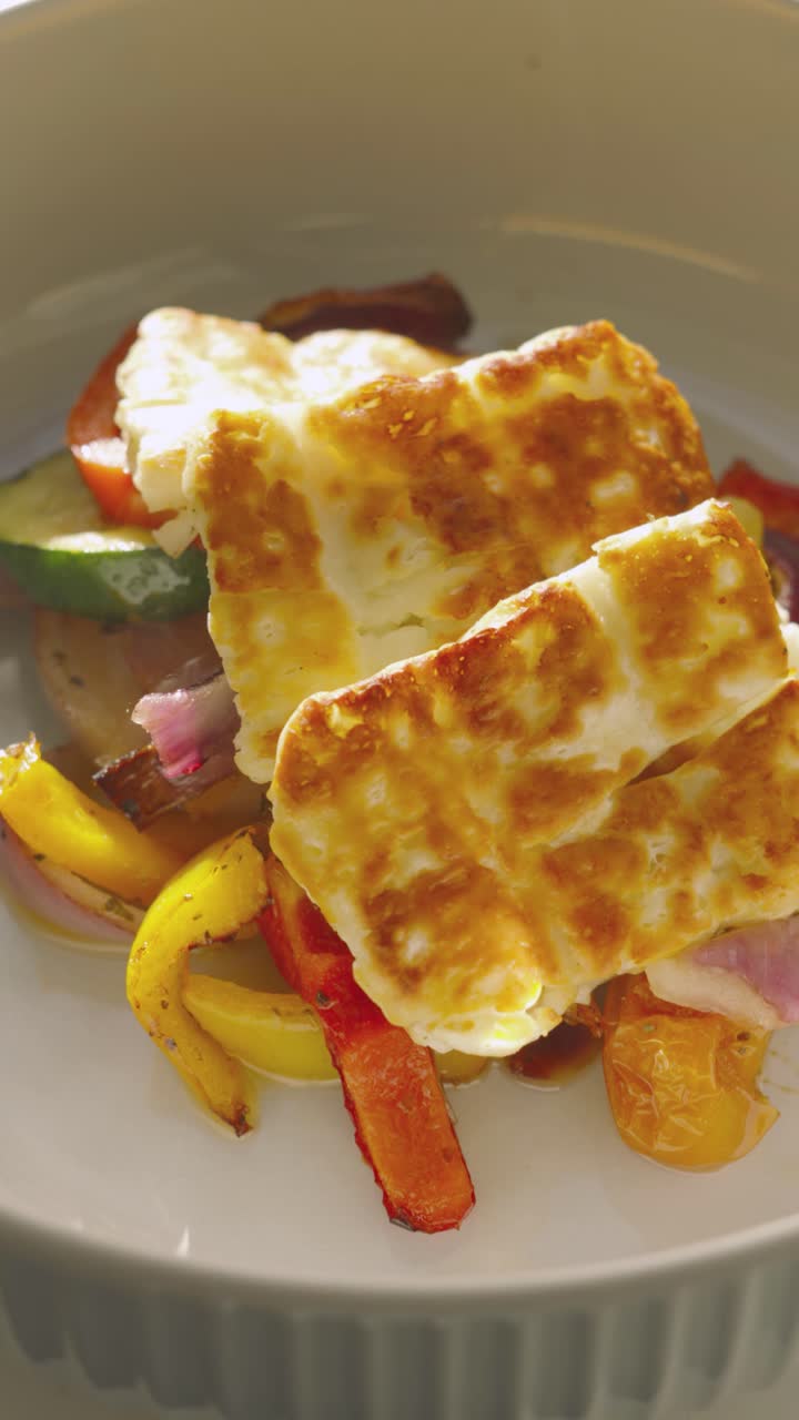 Slow Motion Vertical Video of Freshly Grilled Halloumi Slices Resting on Roasted Mediterranean Vegetables Including Peppers, Courgette, Onions. Healthy Eating Summer Fresh Highly Nutritous Lunch.