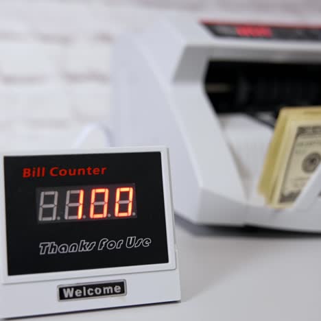 us dollar bills. woman putting money into counting machine at table indoors, close up
