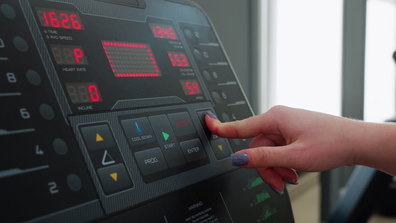 close up hand view of woman with purple nail polish pressing button on treadmill control panel during indoor fitness session showing digital display of time speed and calories burned