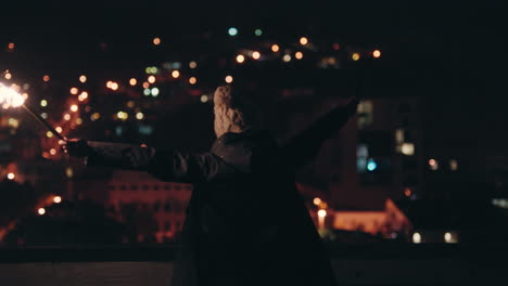 happy caucasian woman holding sparklers dancing on rooftop at night celebrating new years eve enjoying holiday celebration