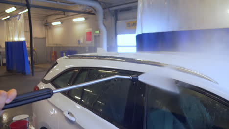 worker spraying water and washing the roof, of a white, suv car, at a carwash, in sweden