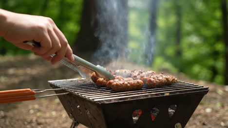 grilling sausages and meat outdoors on a portable barbecue