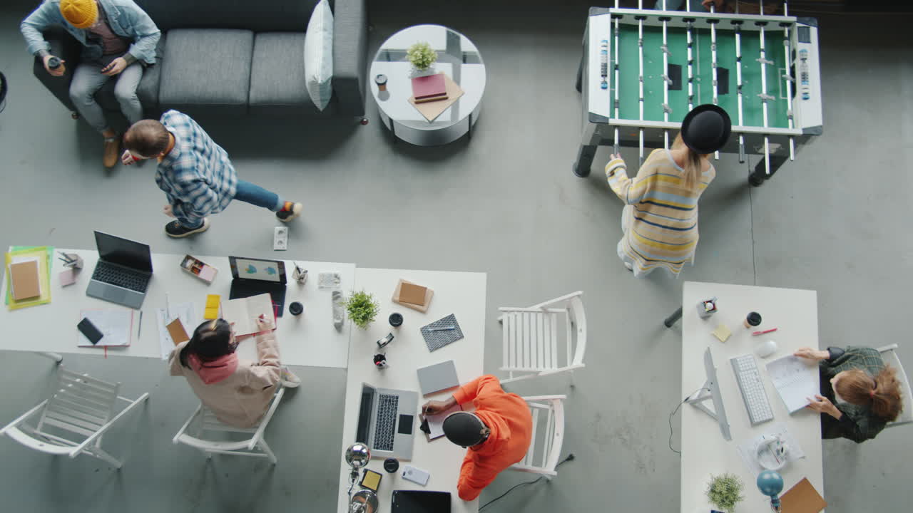 Busy and collaborative office environment with people working, eating, and playing foosball