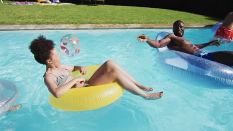 Diverse-group-of-friends-having-fun-playing-on-inflatables-in-swimming-pool