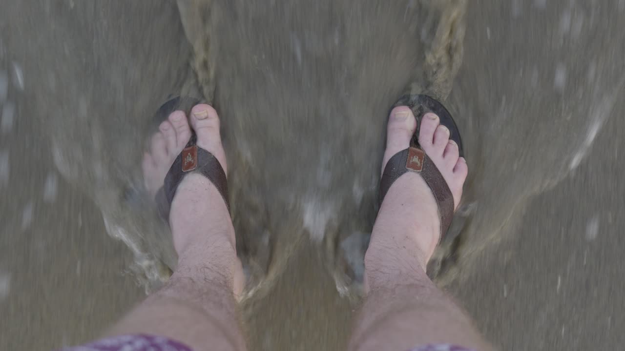 hombres con pies de sandalias se paran en la playa - las olas llegan fácilmente a la playa y cubren los pies