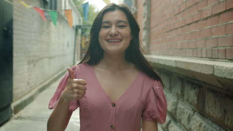 smiling woman in pink dress walking down a city alley