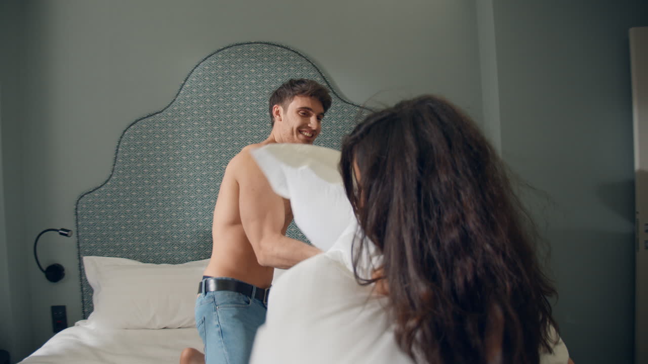 горячая пара шутит на роскошной гостиничной кровати. шикарная пара сражается в подушках в помещении