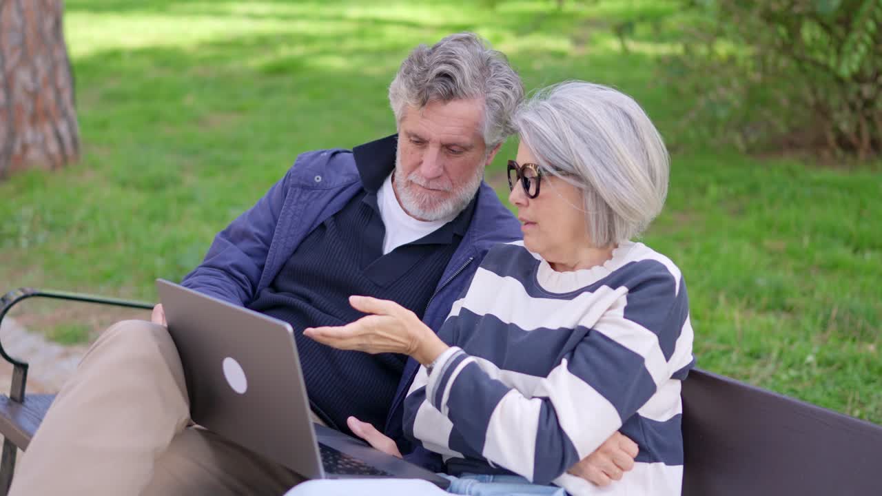 Casal de idosos conversando sobre algo em um laptop no parque