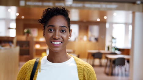 Young-mixed-race-woman-standing-in-a-business-lobby-on-her-way-out-from-work,-looking-to-camera