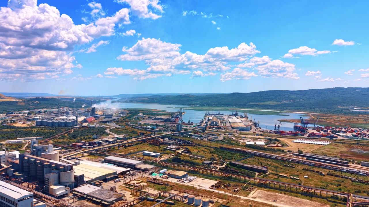 Flyfoto av kystnært industriområde og havn. Produksjonsanlegg og lagringsområder ligger nær en bred vannbukt under en skyet himmel