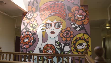 "stay wild" colorful mural with sun shining indoors, woman wearing large hat around flowers - slow motion