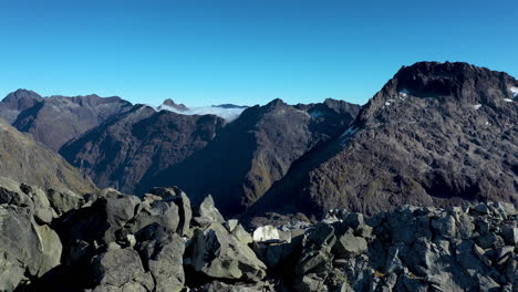 panning-drone-shot-Milford-Sound-Gertrude-Saddle-Fiordland-National-Park,-New-Zealand-hikers-on-top