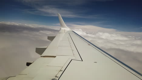 airliner wing entering a thick layer of clouds under a blue sky with sun